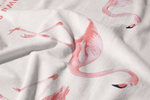 The Flamingo Beach Towel is made of white cotton and features a printed pattern of pink flamingos in various poses. Slightly wrinkled fabric adds soft shadows and texture to this exclusive design.