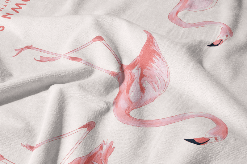 The Flamingo Beach Towel is made of white cotton and features a printed pattern of pink flamingos in various poses. Slightly wrinkled fabric adds soft shadows and texture to this exclusive design.