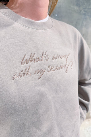 Someone is wearing the WWWMS Embroidered Script Crewneck Sweatshirt in light gray, featuring the phrase “What’s wrong with my sewing?” in cursive on the front.