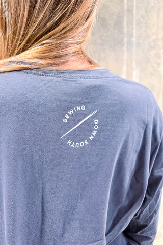 A person with long, light brown hair is wearing the WWWMS Script Long Sleeve Tee featuring comfy long sleeves and white text in Craig's Handwriting that reads SEWING DOWN SOUTH in a circular pattern on the back near the neckline.