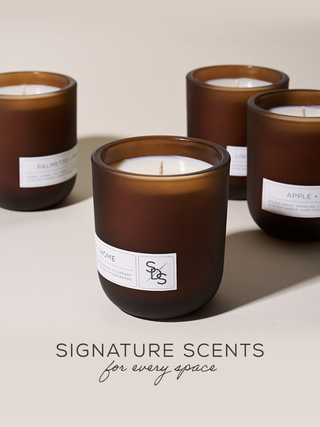 Four brown candles with labels on a light surface, with text 'Signature Scents for every space' below.