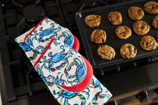 The Crab Craze Mini Oven Mitts, adorned with vibrant blue crab designs, rest by a tray of freshly baked chocolate chip cookies. Their silicone grip ensures safety while bringing the charm of a true crab theme to your kitchen.
