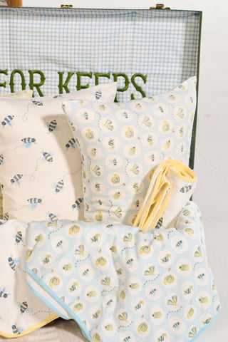 Buggin’ Out Children’s Sleeping Pillow Cover features bee and floral patterns in soft pastels on blue gingham, embroidered with green letters—perfect for a cozy bedtime look.