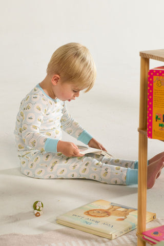A young child in the Buggin’ Out Dream & Play Two Piece Set sits on the floor reading a book, with more children’s books, a small toy nearby, and a wooden bookshelf partially visible on the right.