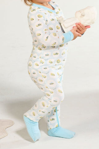 A young child wearing a Buggin’ Out Dream & Play Zipper Romper with hand-drawn bug print holds a white baby doll while standing on a light-colored floor.