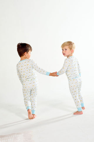 Two children in Buggin’ Out Dream & Play Two Piece Set pajamas hold hands, standing barefoot on a light floor with a plain white background, looking towards the camera.