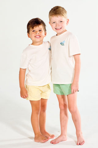 Two boys smiling and standing with their arms around each other, both wearing white Bee You Short Sleeve Children’s Tees with a small bee graphic and colorful shorts.