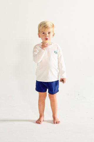 A young child wears a Bee You Long Sleeve Children’s Tee with a bee graphic and blue shorts while holding a lollipop.