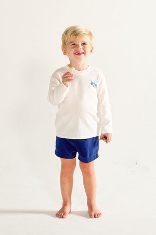 A young child wears a Bee You Long Sleeve Children’s Tee featuring a hand-drawn bee graphic with blue shorts against a white background.