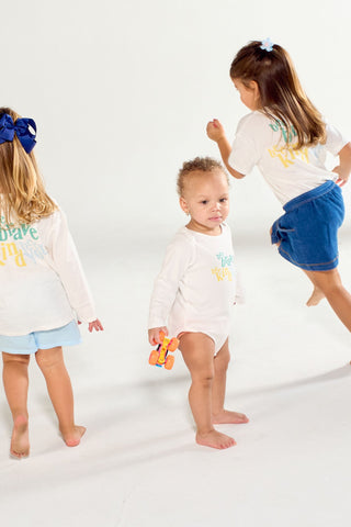 Three children in long-sleeve Bee You Long Sleeve Onesie outfits with colorful text prints playing in a white studio.