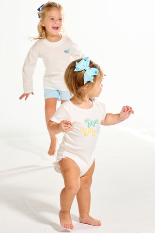 A toddler wears a white short-sleeve Bee You Short Sleeve Onesie with bee brave and bee kind on the front, while a girl runs in the background.