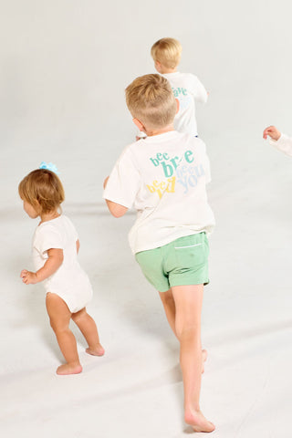 Four children walk across a white background, three of whom are wearing Bee You Short Sleeve Children’s Tee shirts with bee brave and bee you printed on the back.