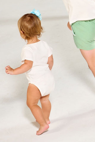 Four children walk across a white background wearing Bee You Short Sleeve Onesie baby clothing with bee-themed graphics and text.