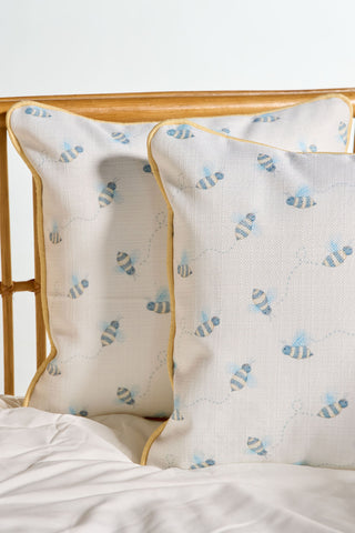 Two white Buzzin’ Around Children’s Pillows with yellow piping sit against a light wooden headboard on a white bed, perfect for children’s decor.