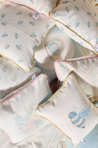 A Bee You Children’s Lumbar Pillow, made in the USA, features soft pastel colors and whimsical bee-themed designs with double-sided prints for added charm—perfect as a decorative accent on a bed.