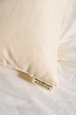 A close-up of the Organic Children’s Sleeping Pillow in a cream color, featuring a fabric tag that reads Sewing Down South, Created With Care, resting on coordinating bedding. This pillow is made with hypoallergenic materials to provide comfort and safety for children while they sleep.