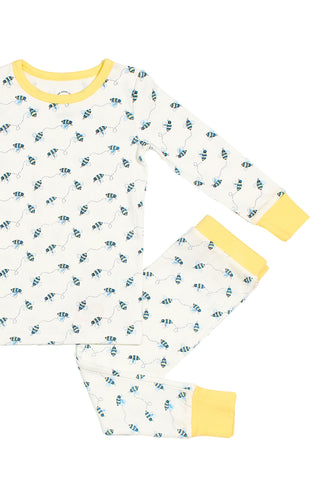 Children’s sleepwear featuring the Buzzin’ Around Dream & Play Two Piece Set—white cotton modal pajamas with blue bee print, yellow trim, long-sleeve top and matching pants, shown flat on a white background.