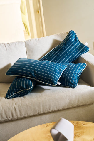 A beige sofa features the Courtyard Stripes Extended Lumbar Pillow from the Core Collection, along with a floral pillow cover. In front sits a light wood table, and a partially open door is visible in the background.