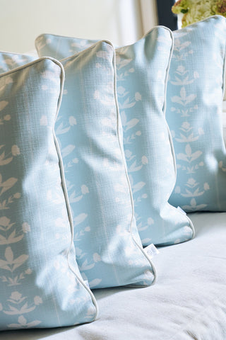 Four light blue Garden Party Pillows with white floral patterns from the Broad Street Blooms Core Collection are arranged in a row on a light-colored couch or bed, adding a soft and cozy atmosphere.