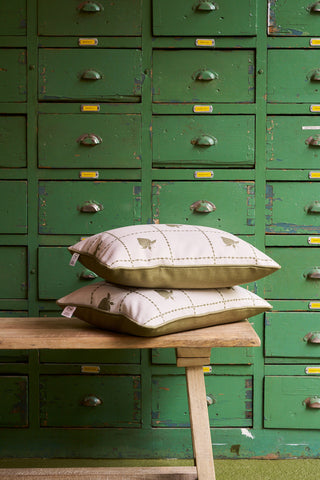 The Strawberry Stitch Grid Lumbar Pillow from the Core Collection sits on a wooden bench in front of vintage green drawers with metal handles and yellow labels, bringing Broad Street Blooms charm to your home.