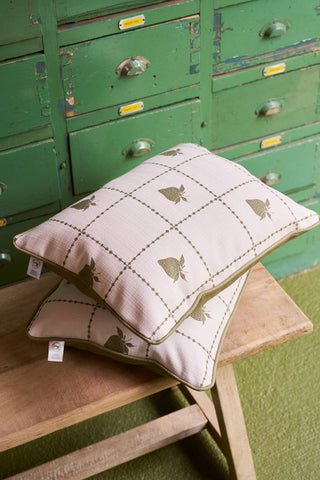 Two decorative pillows—one with Broad Street Blooms and the other, the Strawberry Stitch Grid Lumbar Pillow—rest on a wooden bench. Behind them sits an old green cabinet with drawers and yellow label holders.
