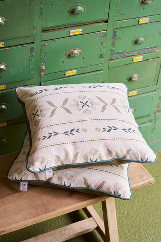 Two Grandmillenial Garden Pillows with floral covers sit on a wooden bench before green vintage drawers with yellow labels, adding cozy, rustic charm. Part of the Broad Street Blooms Core Collection.