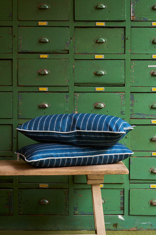 A Courtyard Stripes Extended Lumbar Pillow from our Core Collection sits on a wooden bench in front of a green vintage cabinet with small drawers and metal handles.
