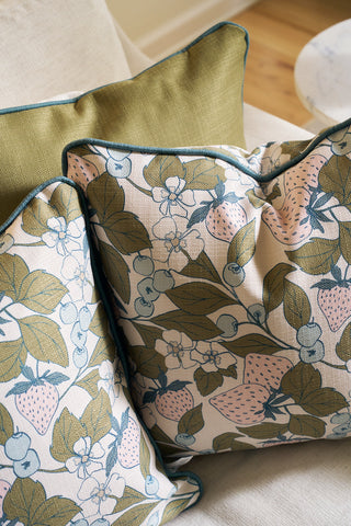 Two decorative pillows rest on a light couch: one in green and the other—the Fruit Fields Pillow—showing a charming botanical design, ideal as accents for garden decor or fans of floral pillow covers.