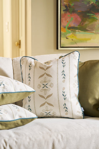 A close-up of a beige sofa with patterned throw pillows; the central floral pillow from our Core Collection is the Grandmillenial Garden Pillow in Broad Street Blooms, flanked by an olive green pillow. A colorful painting hangs behind.