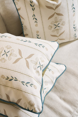 Close-up of two cream-colored Grandmillenial Garden Pillows from the Core Collection, featuring light brown and green floral covers with blue piping, resting on a matching cream fabric surface.
