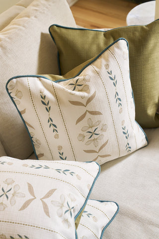 Two Grandmillenial Garden Pillows from the Core Collection, featuring Broad Street Blooms floral covers in beige, blue, and green, are placed on a light sofa with a solid olive green pillow in the background.