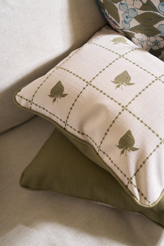 A Strawberry Stitch Grid Lumbar Pillow rests on a light couch above a solid green pillow, while a Broad Street Blooms floral pillow cover is visible in the background.
