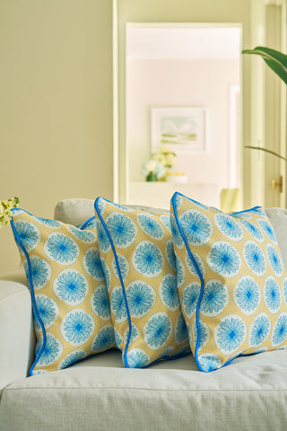 Three beige pillows with blue floral patterns and piping evoke a coastal vibe on a pale sofa, while the Yellow Calico Scallops Pillow stands out as an elegant statement in the bright, modern living room.