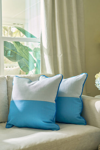 Two Spring Blue Blocks Oversized Pillows rest on a light sofa near a sunny window. Large green leaves and sheer curtains add a calming, modern feel to the bright, cozy space.