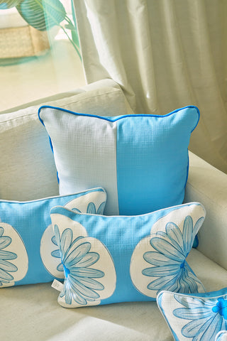 A white couch is styled with blue and white pillows, including the Calico Scallop Lumbar Pillow and a large two-tone square pillow, for a sophisticated, summer-inspired look. Sunlight filters through sheer curtains in the background.