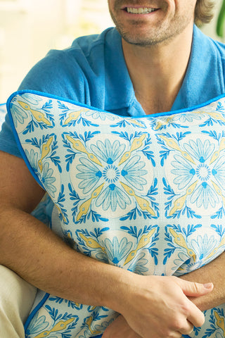 A man in a blue shirt smiles while hugging the Euro Blue Tiles with Spring Blue Stripe Pillow, featuring a blue, yellow, and white floral pattern that evokes European charm. Only the lower half of his face is visible.