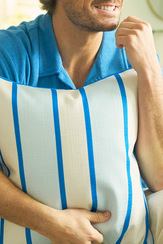 A person in a blue collared shirt smiles while holding the Euro Blue Tiles with Spring Blue Stripe Pillow. The image captures only the lower half of the face and torso, highlighting the pillows European-inspired style.