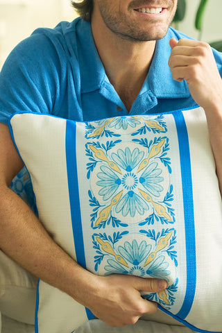 A man in a blue shirt smiles while holding the Line of Euro Blue Tiles Pillow, featuring a blue and yellow floral pattern inspired by Mediterranean villages and classic European elegance.