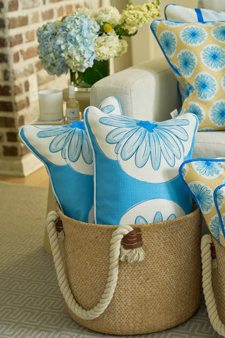 A woven basket with rope handles holds two blue and white floral pillows, adding sophistication. The Calico Scallop Lumbar Pillow in a similar design rests on a cream sofa, while hydrangeas on the table evoke coastal summers.