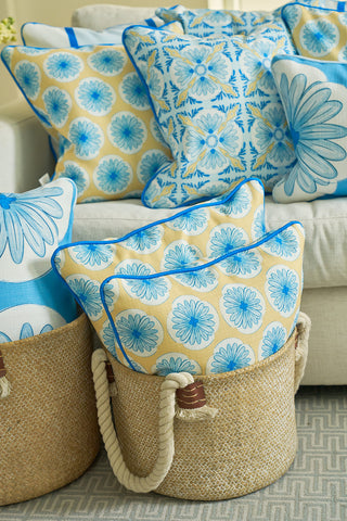 The Yellow Calico Scallops Pillow, featuring blue and beige floral patterns, is arranged on a beige sofa and in rope-handled woven baskets for a cozy coastal vibe and an elegant statement.
