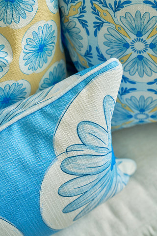 The Calico Scallop Lumbar Pillow, featuring large stylized floral designs in blue and yellow, is arranged with two matching decorative pillows on a light fabric surface, adding a sophisticated, coastal-inspired touch.