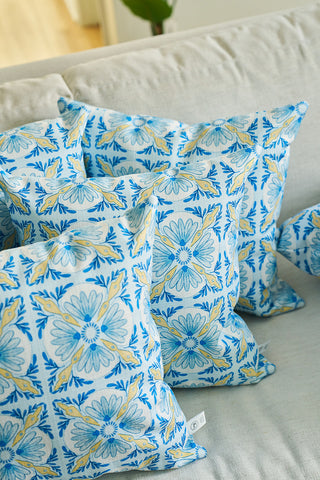 Four Euro Blue Tiles Pillows, featuring a blue, yellow, and white floral design, are displayed on a light sofa, adding a cozy and inviting touch as the perfect accent piece for any home.