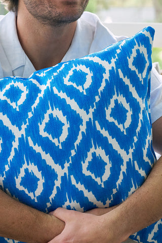 A person in a light blue shirt hugs the Blue Ikat Pillow, featuring a bold blue and white geometric pattern. Their face is partially out of frame.