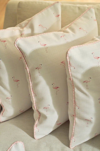 Three Flamingo Scatter Oversized Pillows, featuring white fabric with pink piping and small hand-drawn flamingos, are arranged on a light beige sofa.
