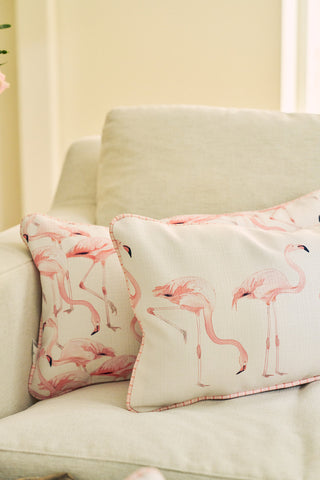 A Flamingo Cluster Extended Lumbar Pillow adds coastal charm to a light beige sofa in a softly lit room, featuring pink flamingo prints in the Sewing Down South® pattern.