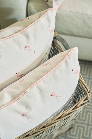 Two white Flamingo Scatter Oversized Pillows featuring small pink flamingo prints and elevated twisted welt rest in a woven basket, with a beige couch and patterned rug visible in the background.