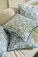 The Blue Lattice Oversized Pillow, crafted from durable fabric with a coastal blue geometric lattice pattern of connected hexagons and rectangles, is arranged on a light beige sofa with three other coordinating white throw pillows.