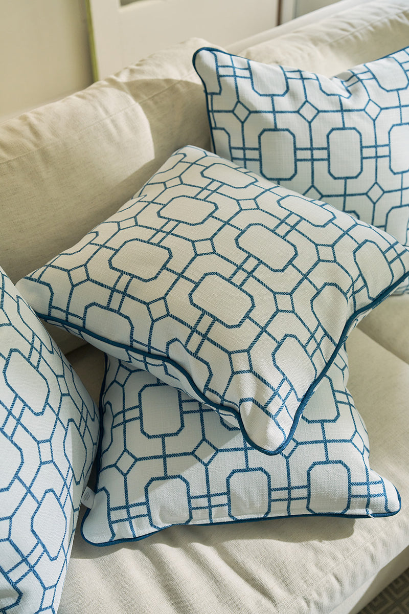 The Blue Lattice Oversized Pillow, crafted from durable fabric with a coastal blue geometric lattice pattern of connected hexagons and rectangles, is arranged on a light beige sofa with three other coordinating white throw pillows.