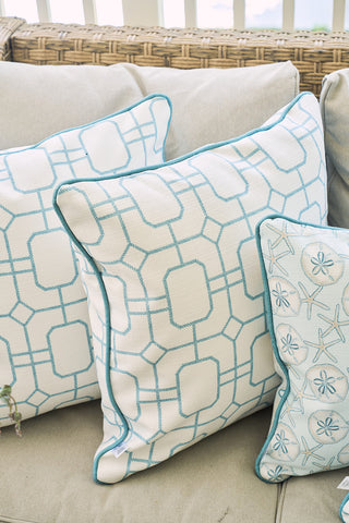 Three decorative pillows on a beige sofa: two with blue geometric lattice prints and one Beach Lattice Oversized Pillow, all set against a wicker backrest for coastal comfort.