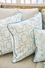 Three decorative pillows on a beige sofa: two with blue geometric lattice prints and one Beach Lattice Oversized Pillow, all set against a wicker backrest for coastal comfort.